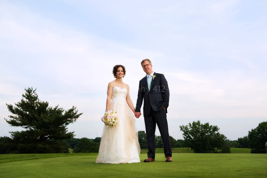 bride and groom stand outside on a golf course on a sunny day