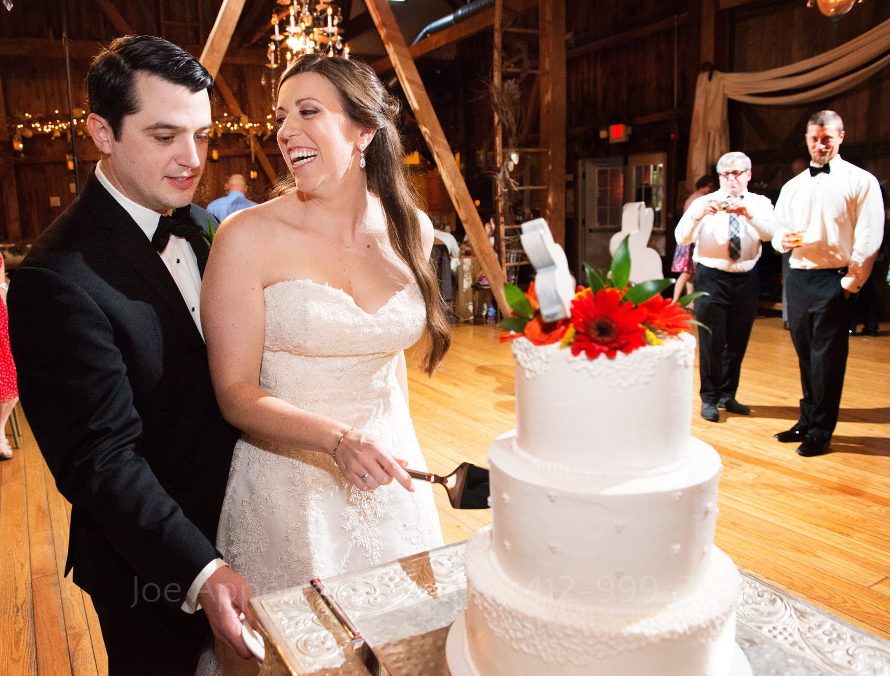 Bride and groom stand next to each other as they cut their wedding cake. bride looks over at groom during their Chanteclaire Farm Wedding.
