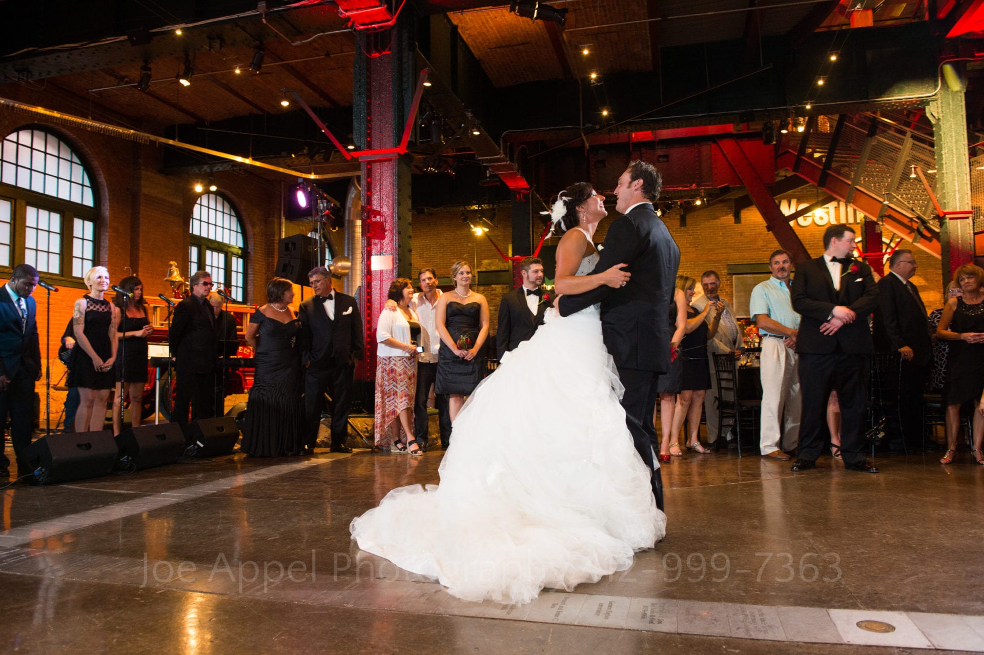 A couple dances, the bride wearing a puffy white dress the groom a black tuxedo in the Great Hall at the Heinz History Center.