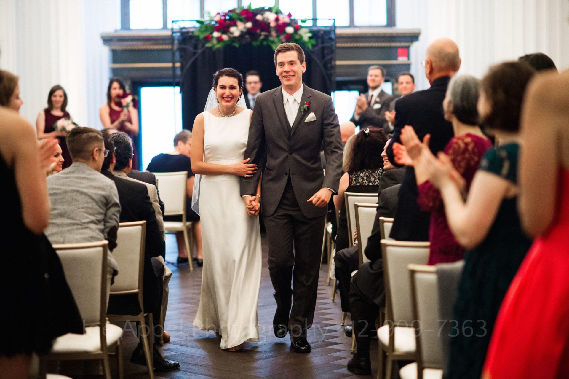 guests applaud a bride and groom as they walk away from their chuppah