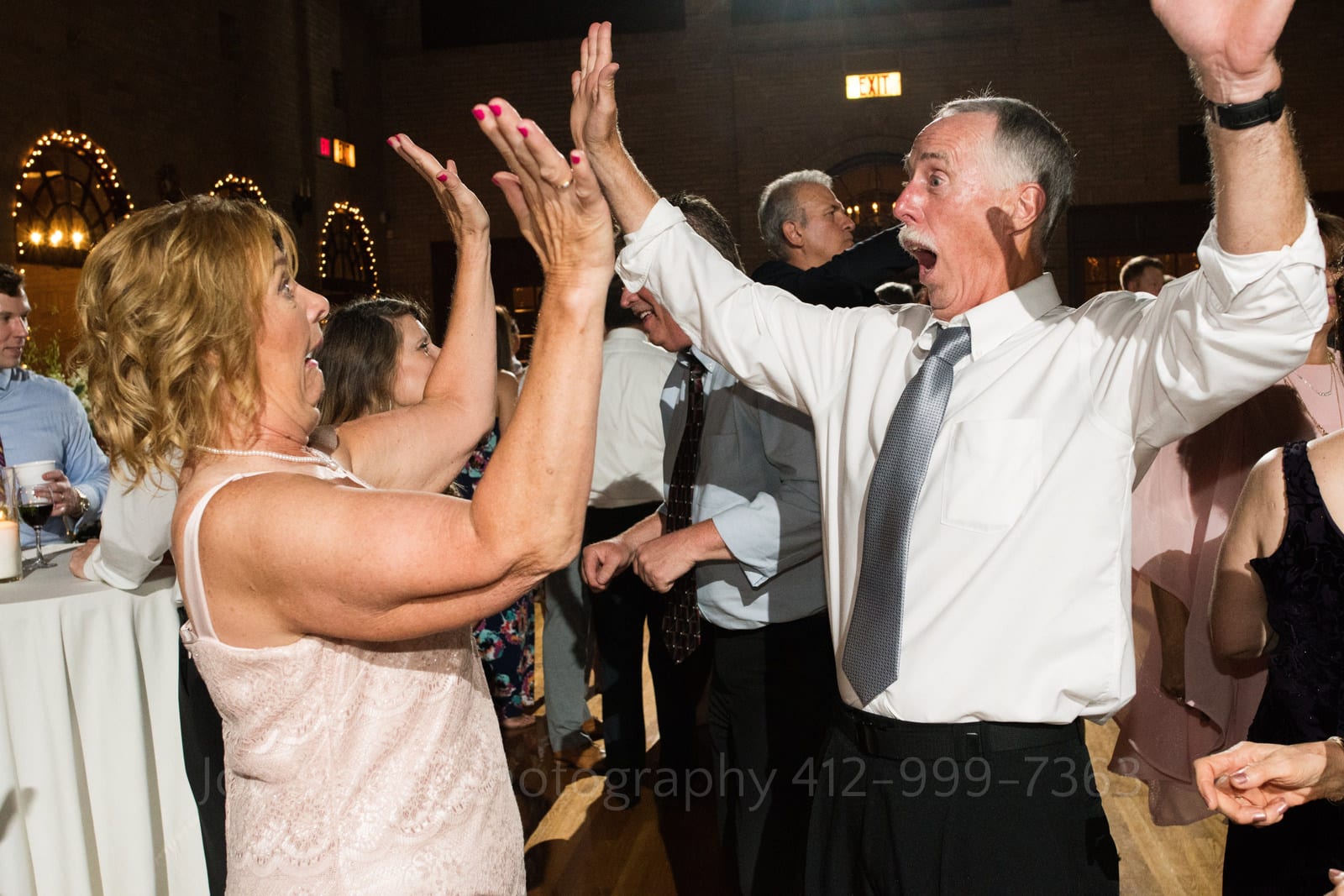 An older man and woman hold their hands in the air and make funny faces at each other while they dance during a St Francis Hall Washington DC wedding.