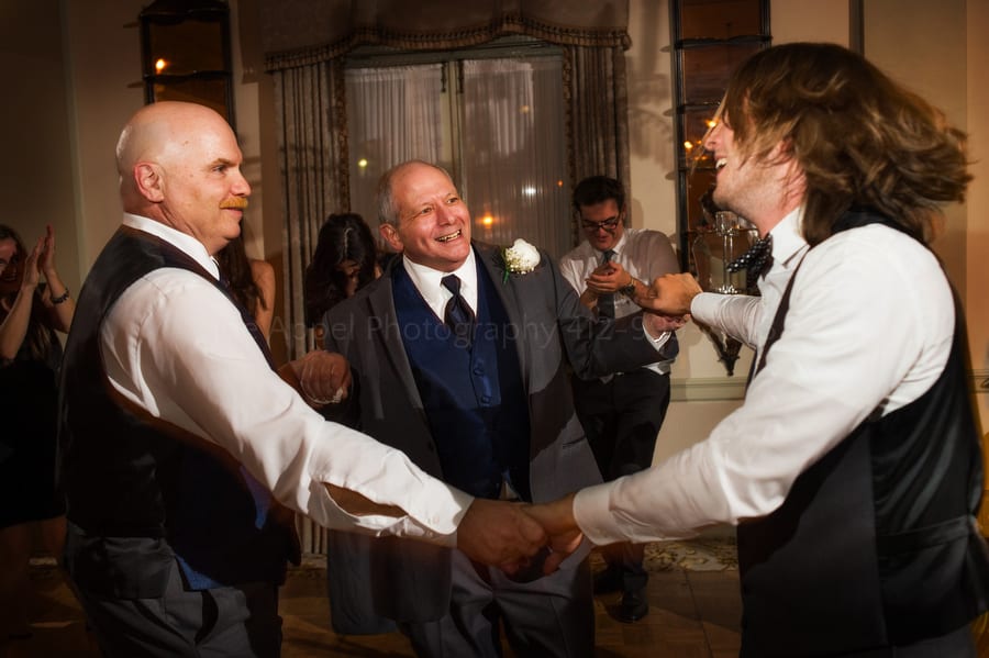 groom dances with his father and his father-in-law during a wedding reception