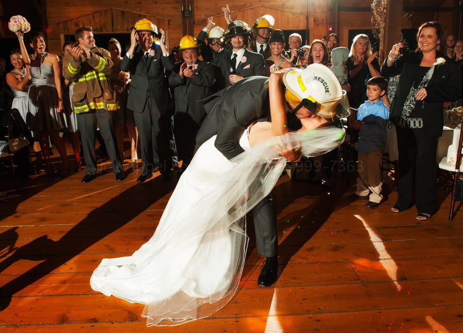 a groom wearing firefighters gear dips his bride as they kiss. Wedding Photography at Lingrow Farm.