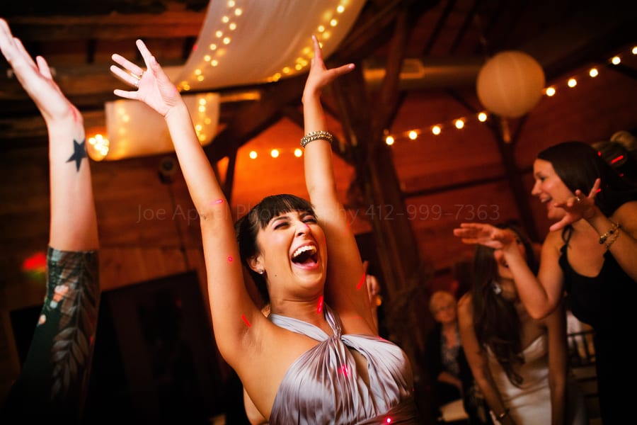 a maid of honor smiles and dances with her arms up at a wedding