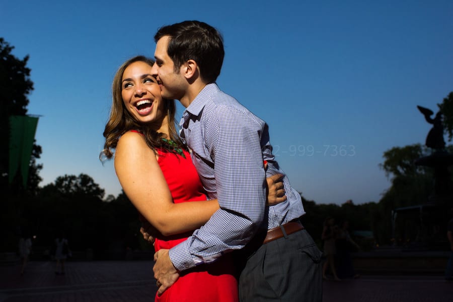 engaged couple laughs as they kiss in central park