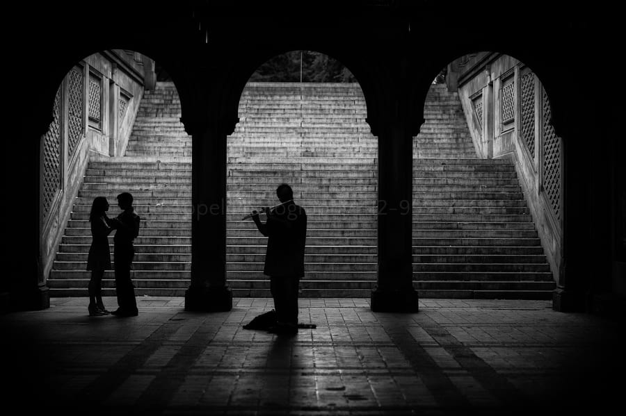 silhouette of a couple dancing beneath the stairs in central park as a man plays flute 