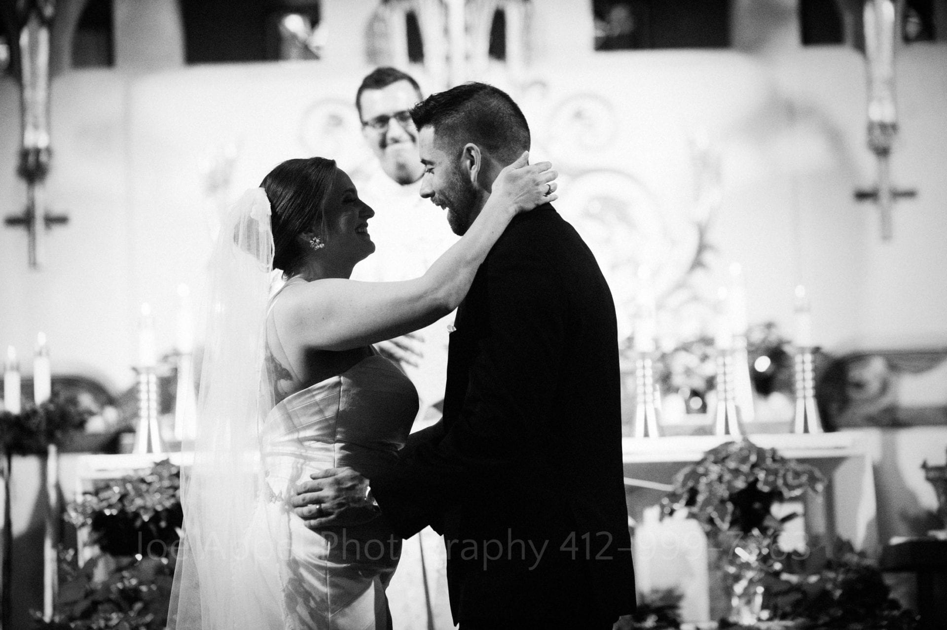 A bride reaches her right arm around the neck of her groom as they move in for a kiss at the end of their wedding ceremony.