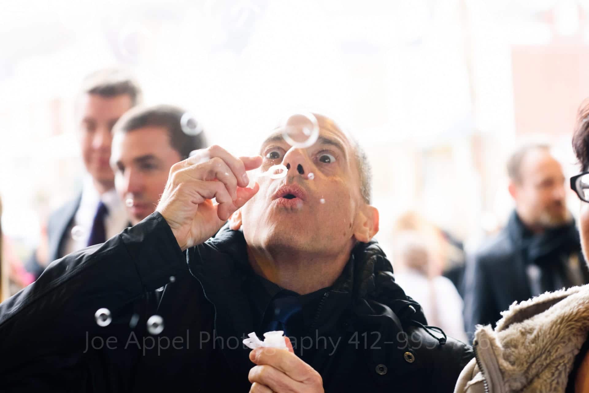 A man's eyes open wide as he focuses on the bubble he's blowing at the end of a wedding.