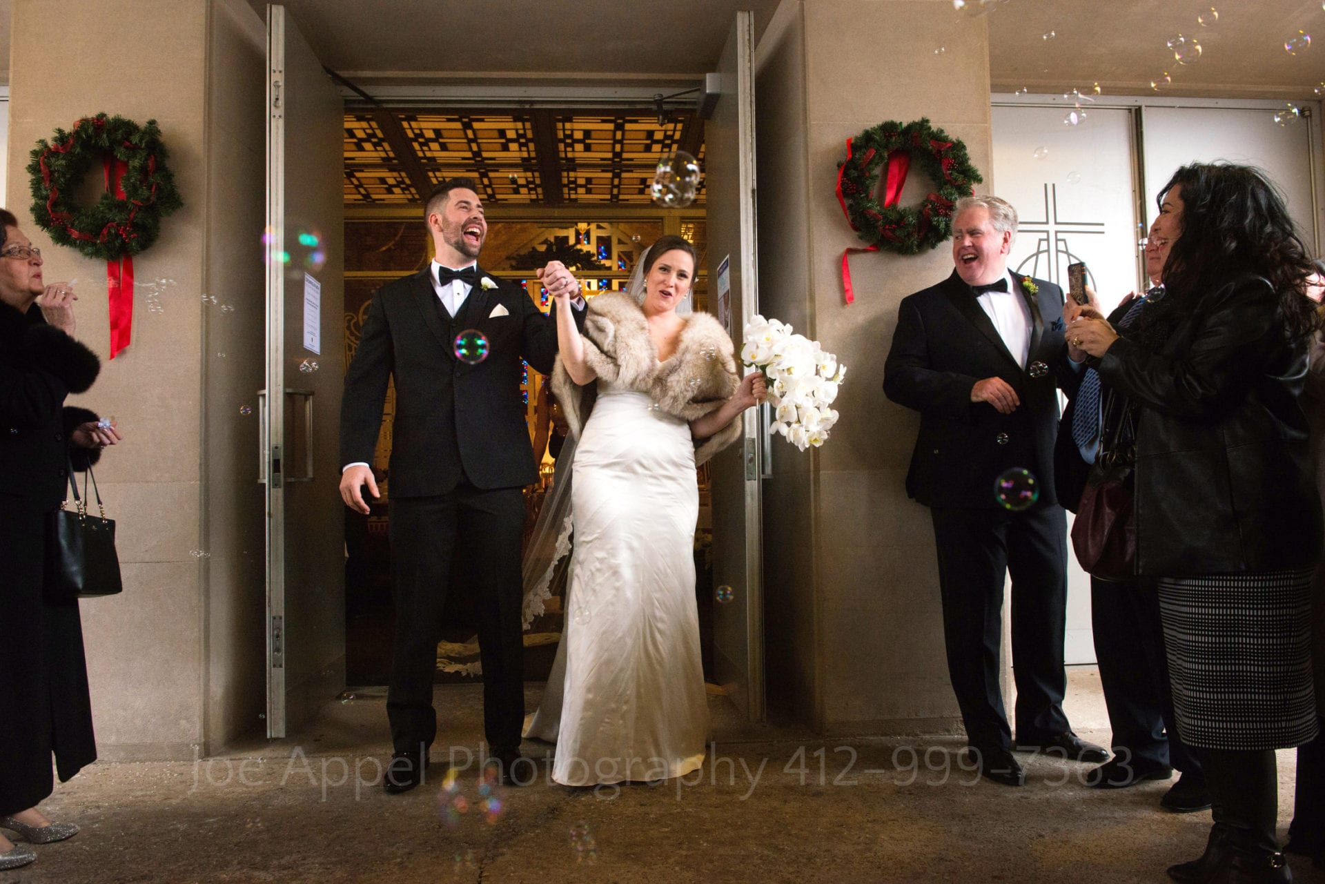 A bride and groom arrive at the door of the church after their wedding and are greeted by their cheering guests who are blowing bubbles.