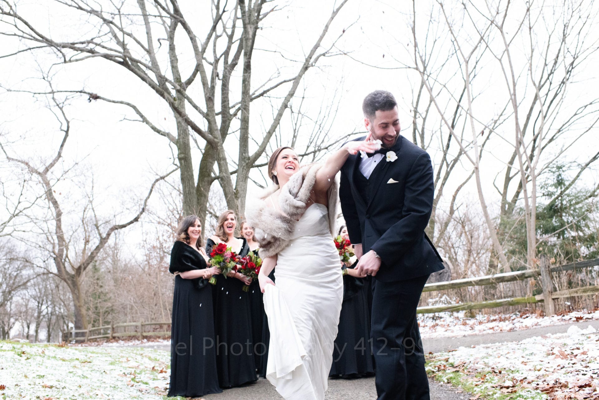 A groom turns his face as his bride smashes a snowball in his face as her bridesmaids laugh.