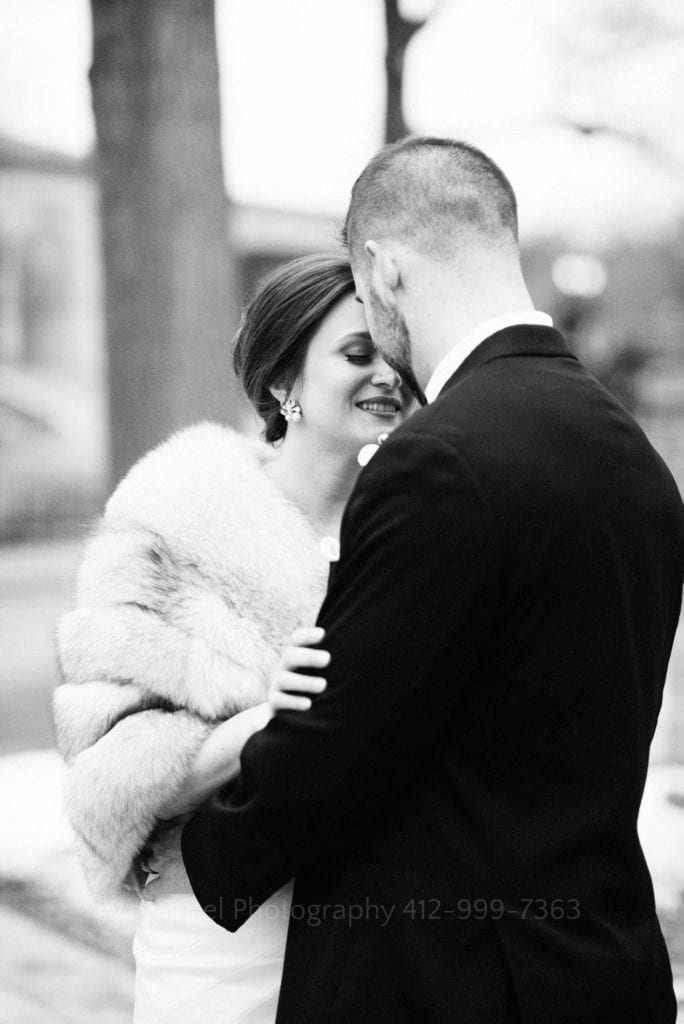 black and white portrait of a bride and groom touching foreheads as they embrace. The groom is facing away from the camera but you can see the bride's smile.