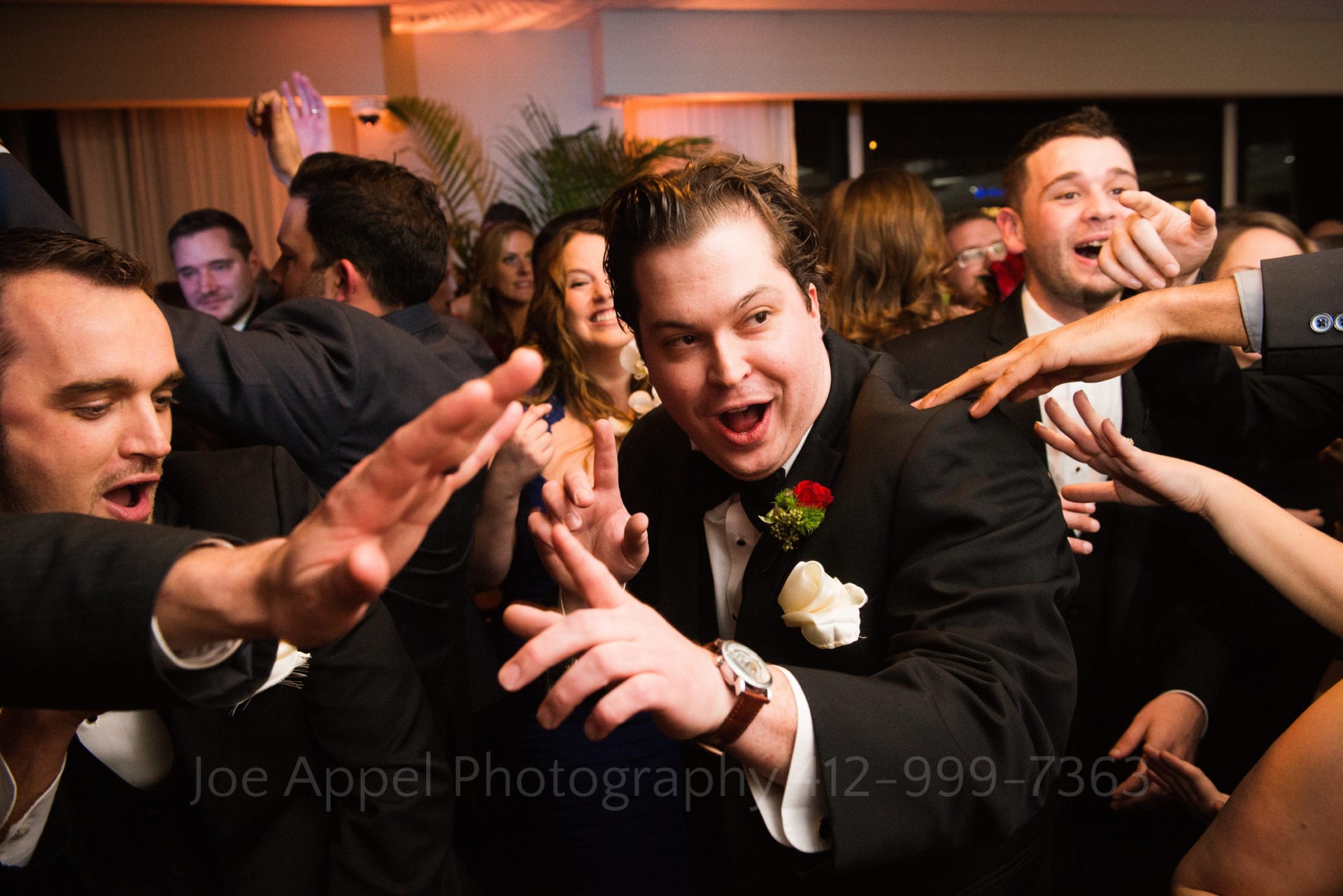 A groomsman dances and smiles while a bunch of hands point towards him.