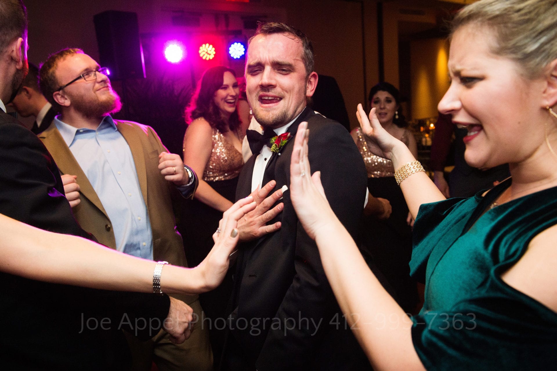 Purple, red, and blue lights shine on a group of people smiling and dancing together at a Renaissance Pittsburgh hotel wedding.