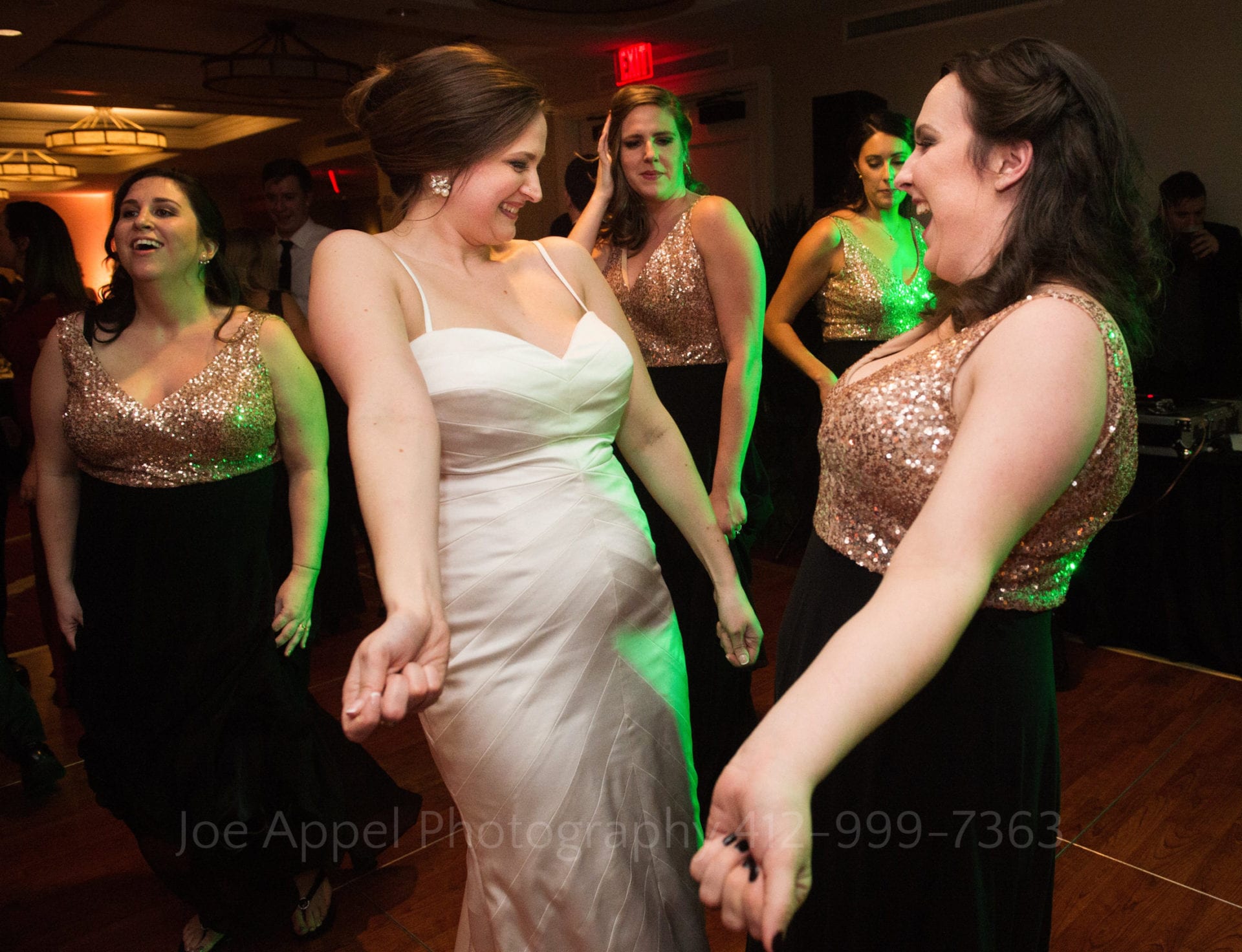 A bride and her bridesmaid hold their hands to their sides and shimmy on the dance floor during a wedding.