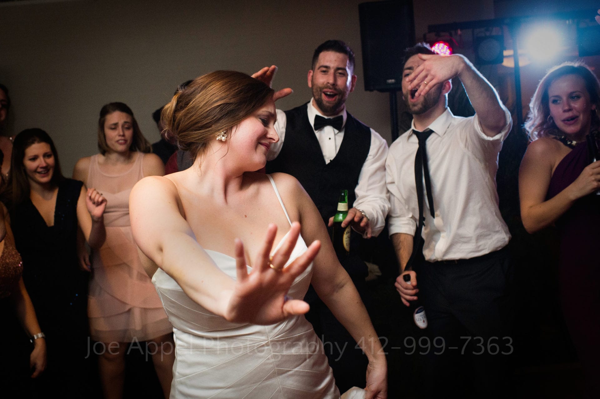 A bride holds her hand out in front of her as she dances in front of a group of cheering guests at her wedding reception.