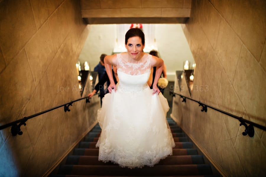 a bride holds her dress as she walks up a flight of stairs
