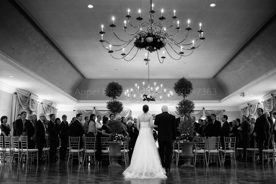 a bride and her father walk down the aisle during a wedding in the grand ballroom at longue vue club