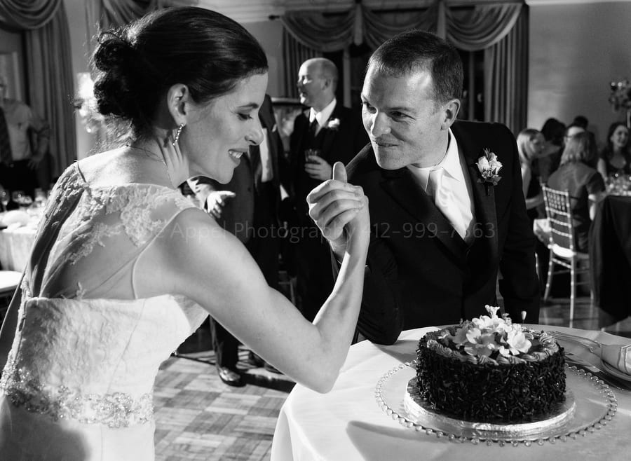a bride and groom arm wrestle before cutting their cake