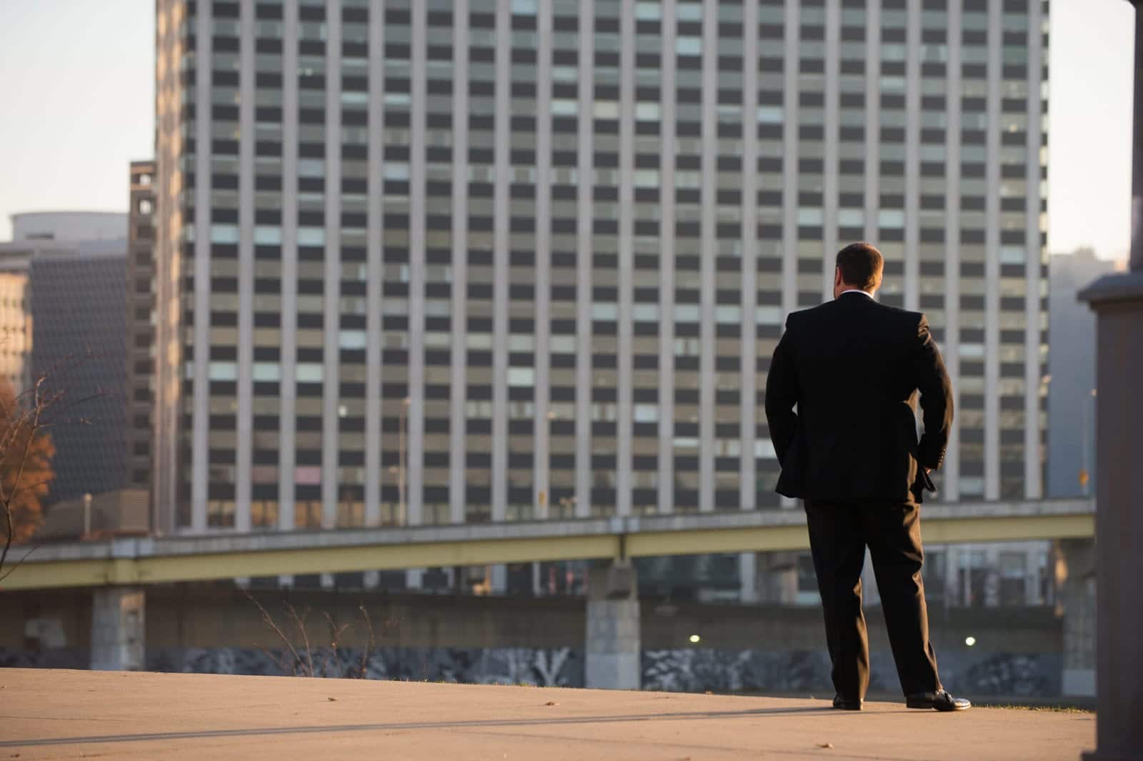 A groom stands on the north shore of the Allegheny River with Gateway Center visible in the background.