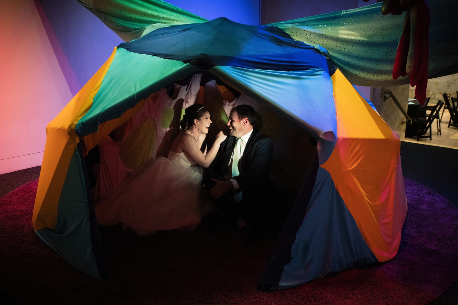 A bride and groom laugh as they sit together inside of a tent before their Children's Museum Pittsburgh Wedding.