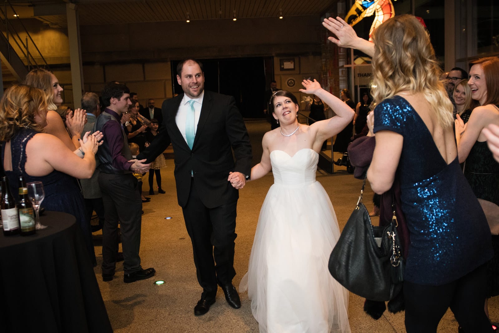 A bride reaches up to give a high five to a guest in a blue dress as she and her groom walk together after their Children's Museum Pittsburgh Wedding.