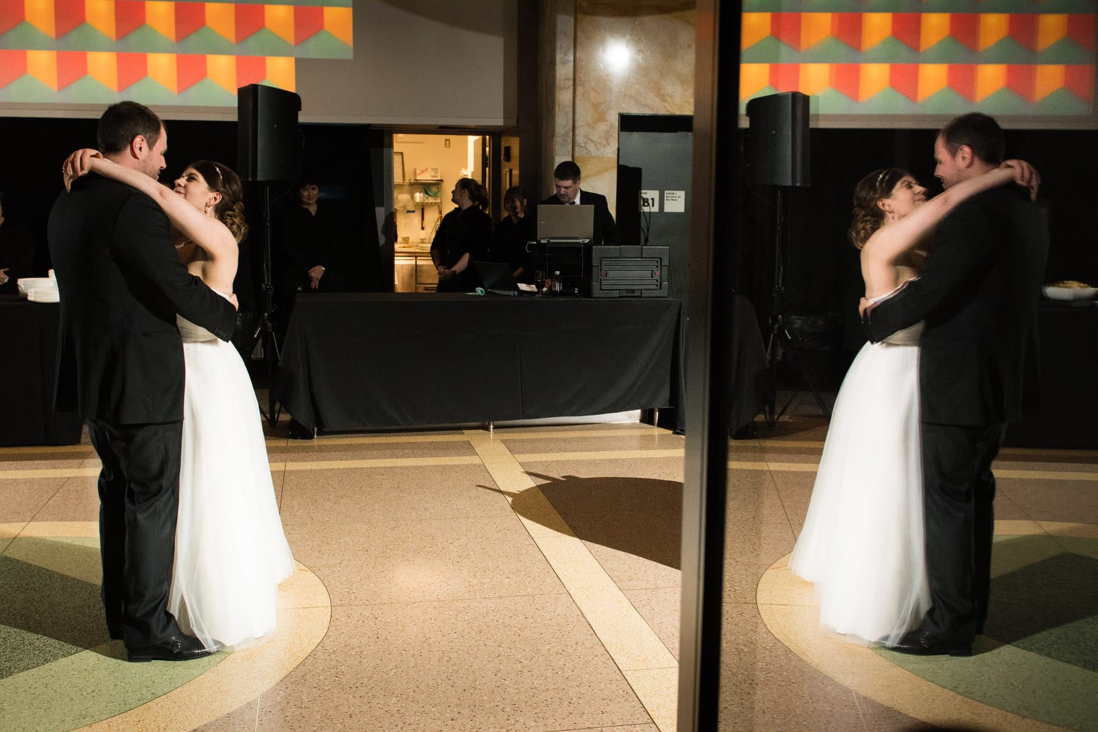 A bride and groom are reflected in a glass door as they have their first dance in the big red room at the Pittsburgh Children's Museum.