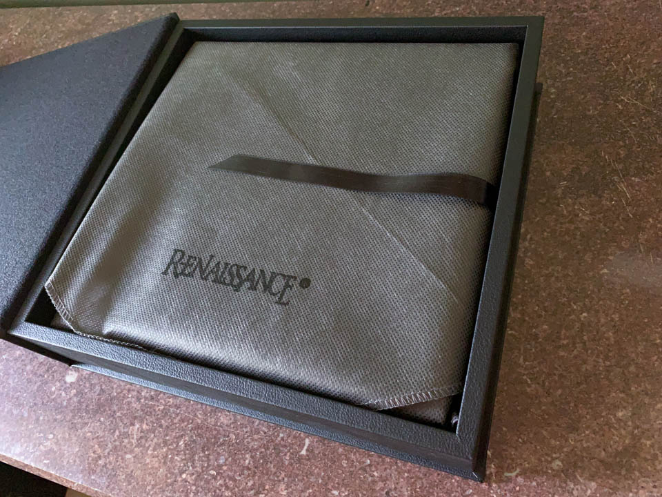 A 10x10 album wrapped in a protective sleeve sits inside of a presentation box with a hinged cover.