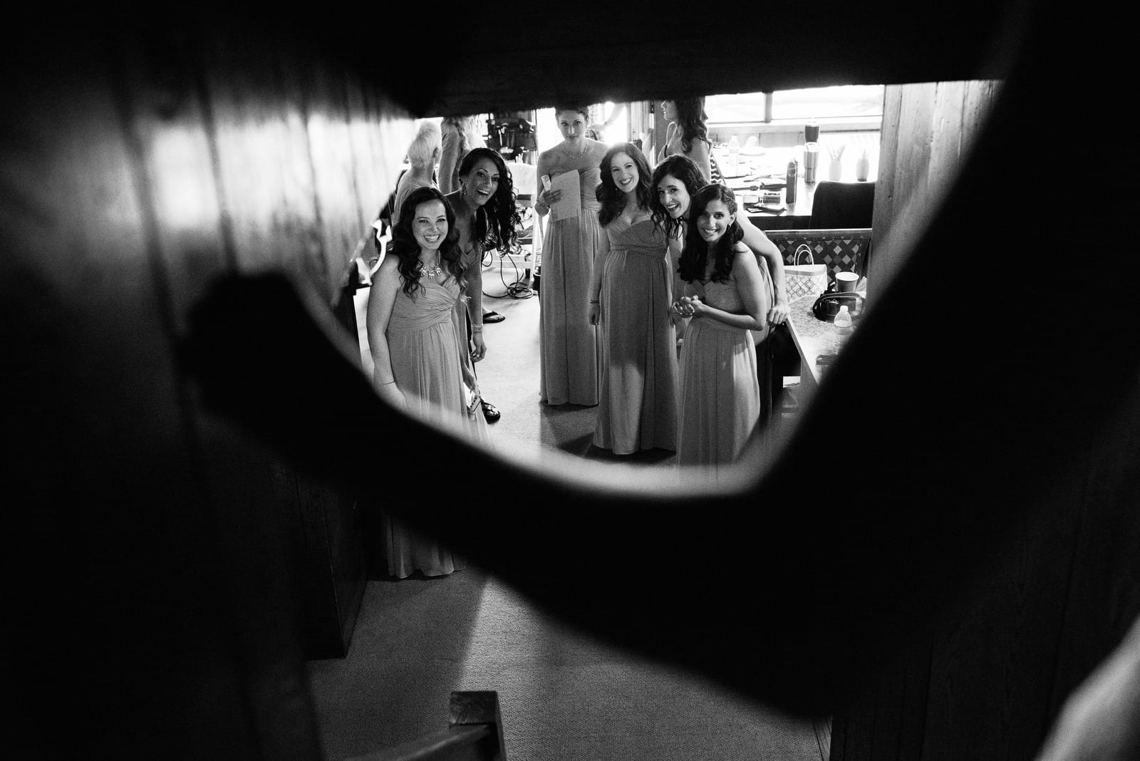 Seen from behind the bride, bridesmaids smile as they see a bride walking down the stairs before her Seven Springs wedding.