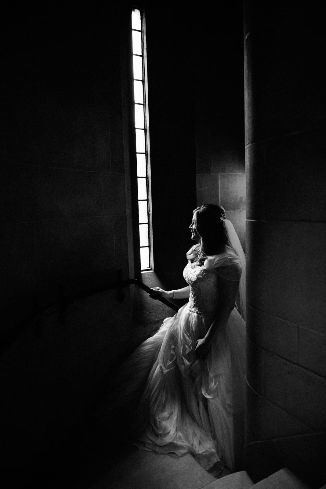 A bride pauses by the long, skinny tall window on the circular stone staircase coming from the basement of Heinz Chapel before her wedding.