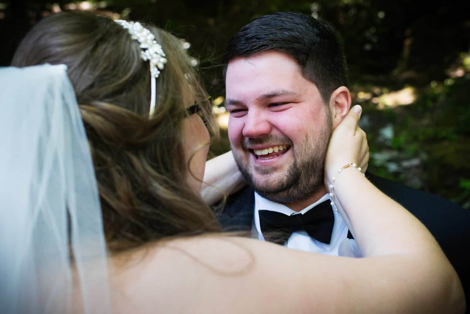A groom grins as his bride holds his head in her hands before their Seven Springs wedding.