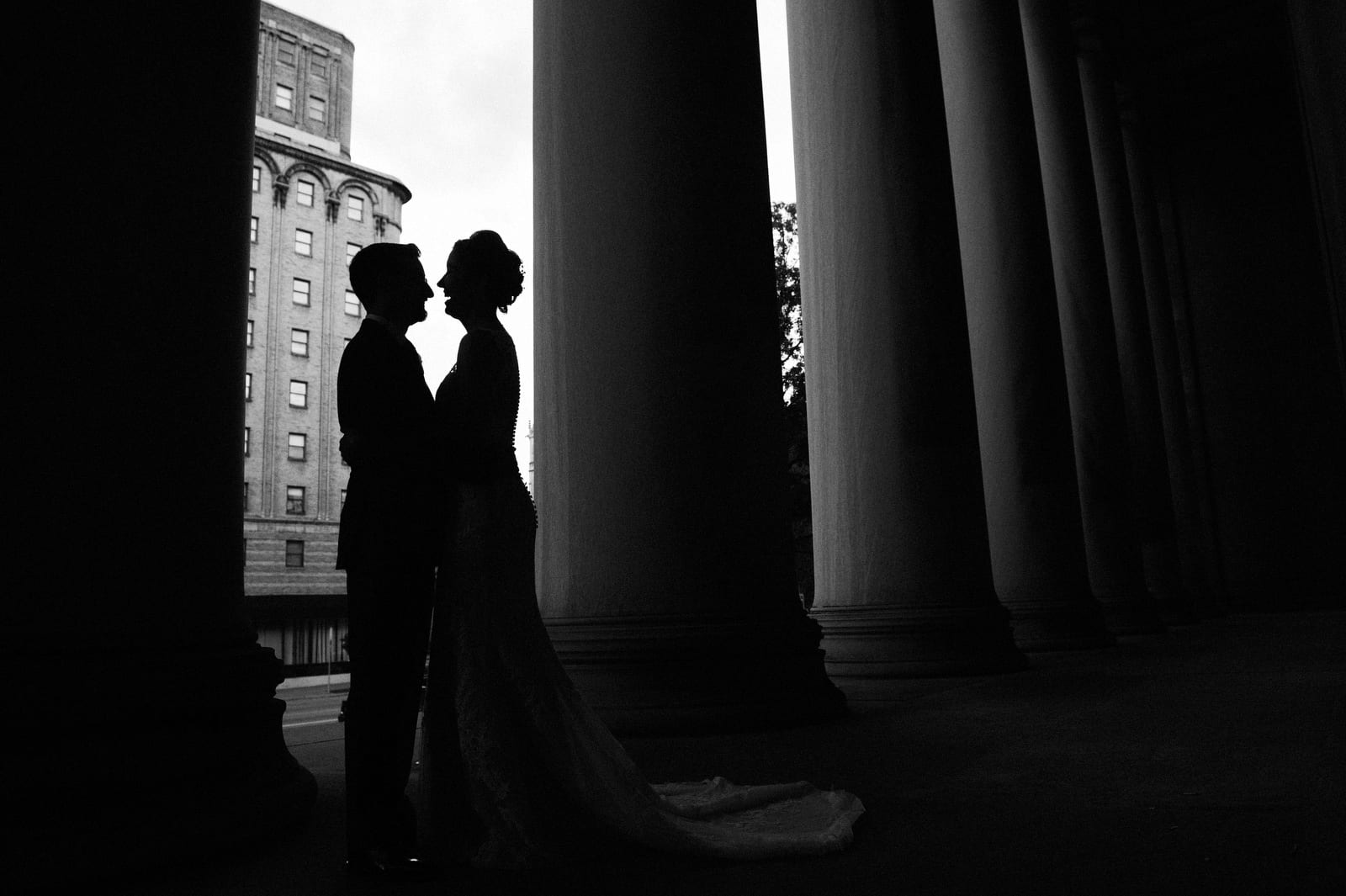 A bride and groom in silhouette between the columns at the Mellon Institute.