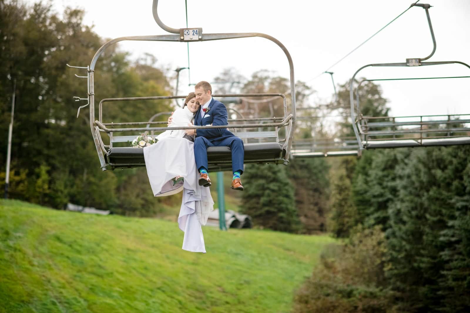 A bride and groom cuddle as they ride a ski lift chair after their Seven Springs wedding.