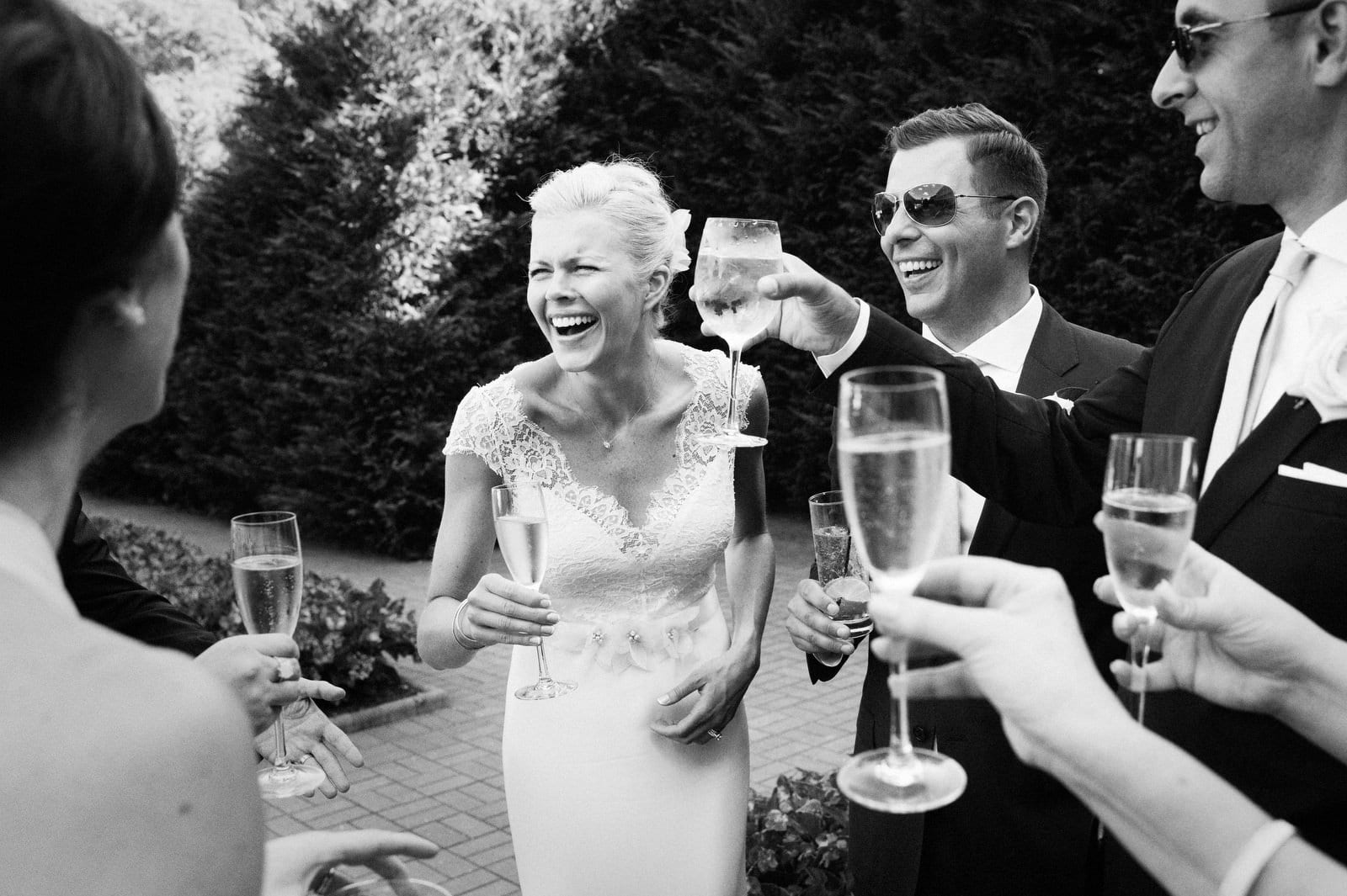 A bride and groom laugh as they hold champagne flutes for a toast on a patio after their wedding at the Omni Bedford Springs resort.