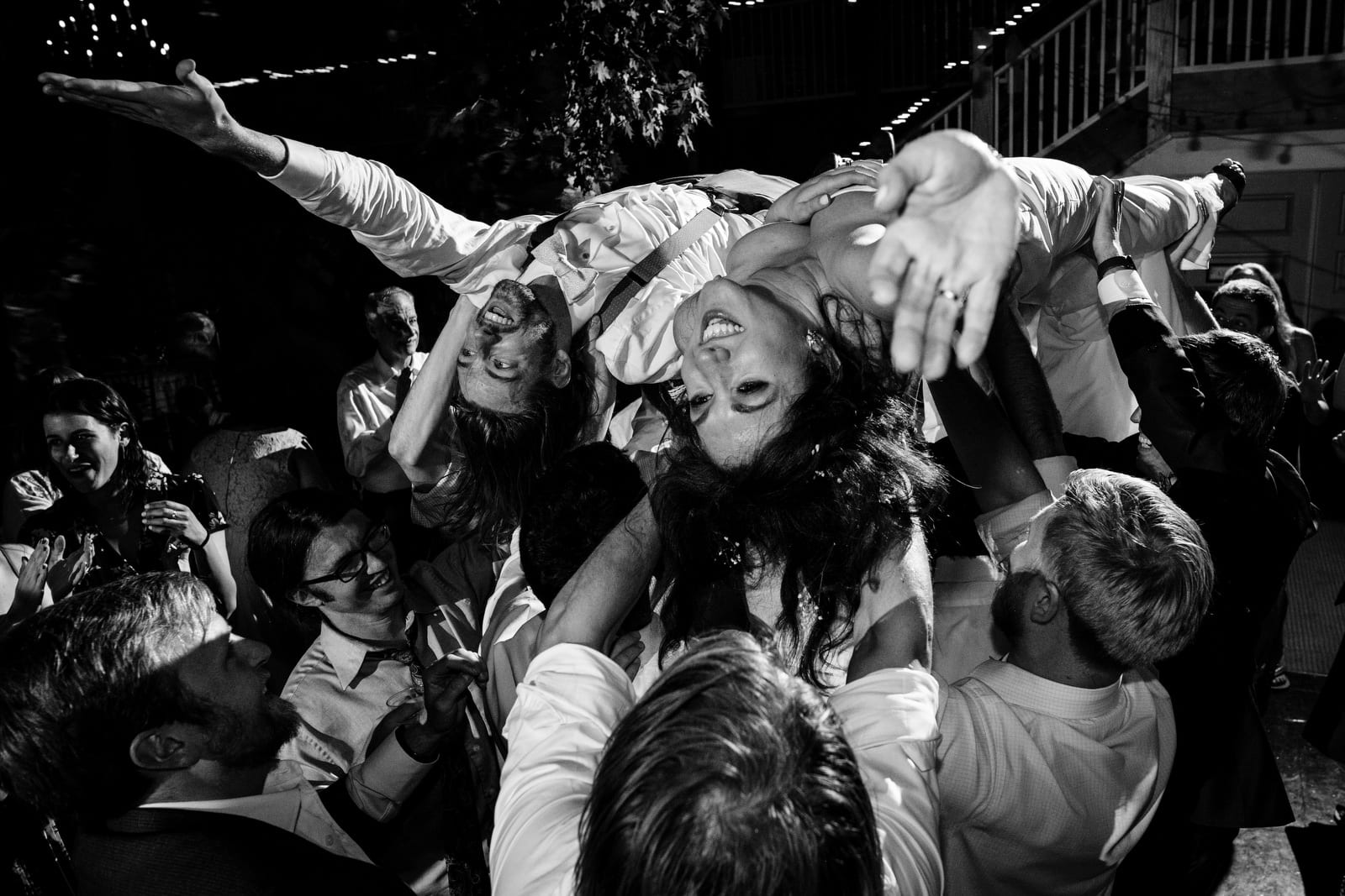A bride and groom hold their hands out as they are lifted upside down by their guests during their reception at The Barn at Gibbet Hill.