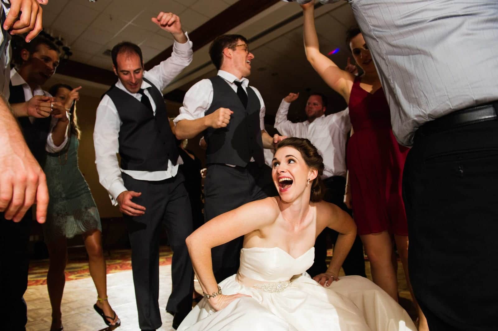 A bride squats low and laughs on the dance floor of her wedding reception at Stonewall Resort in West Virginia.