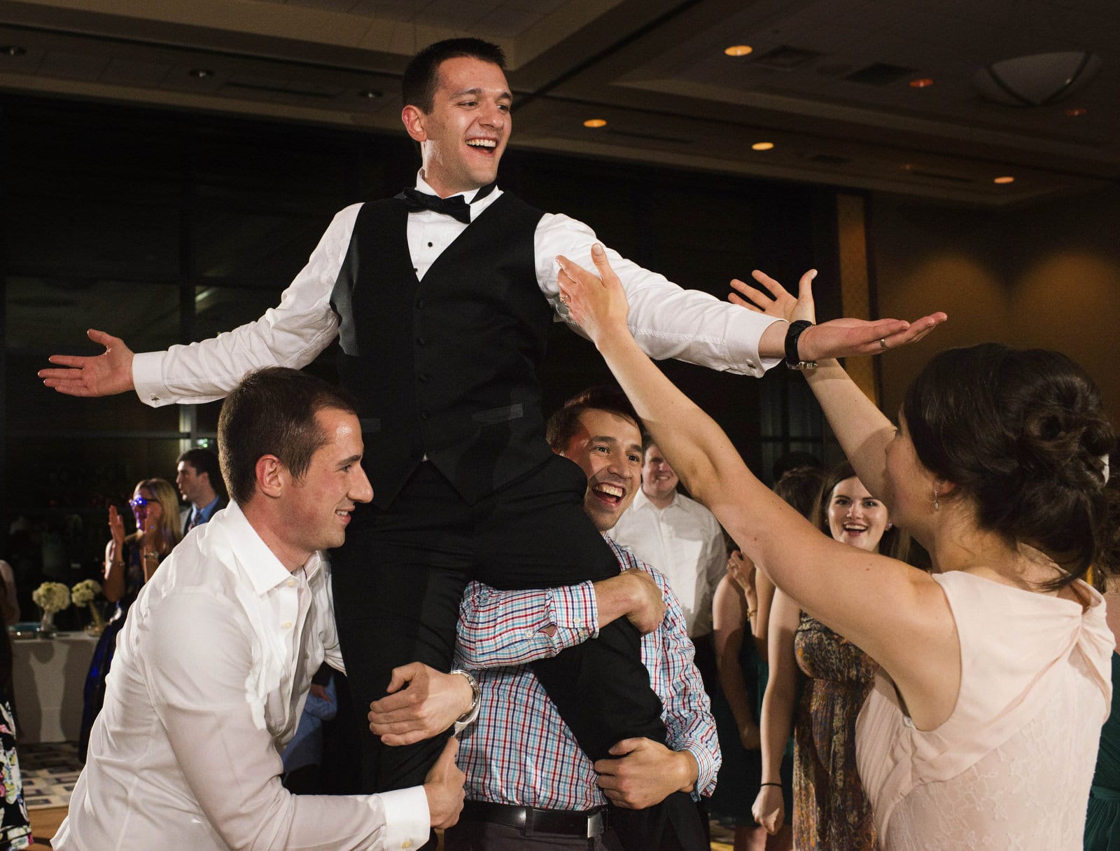 A bride reaches her hands up for her groom who is carried to her by two wedding guests during their reception at the Duquesne University Power Center.