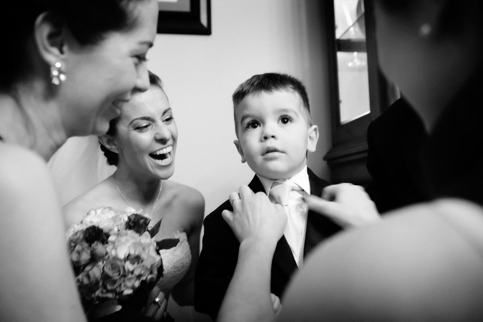 A bride laughs as she kneels next to a young ring bearer who has his tie adjusted by his mother at St. Stanislaus Church in the Strip District.