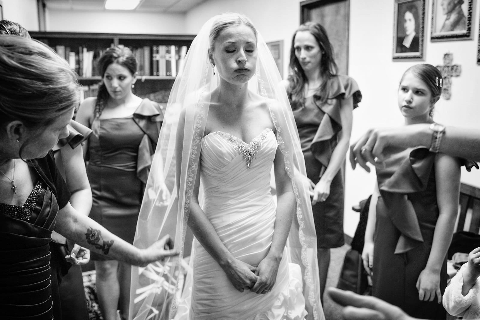 A bride closes her eyes and puffs out a breath as worried looking women stand around her before her wedding at Duquesne University Chapel.