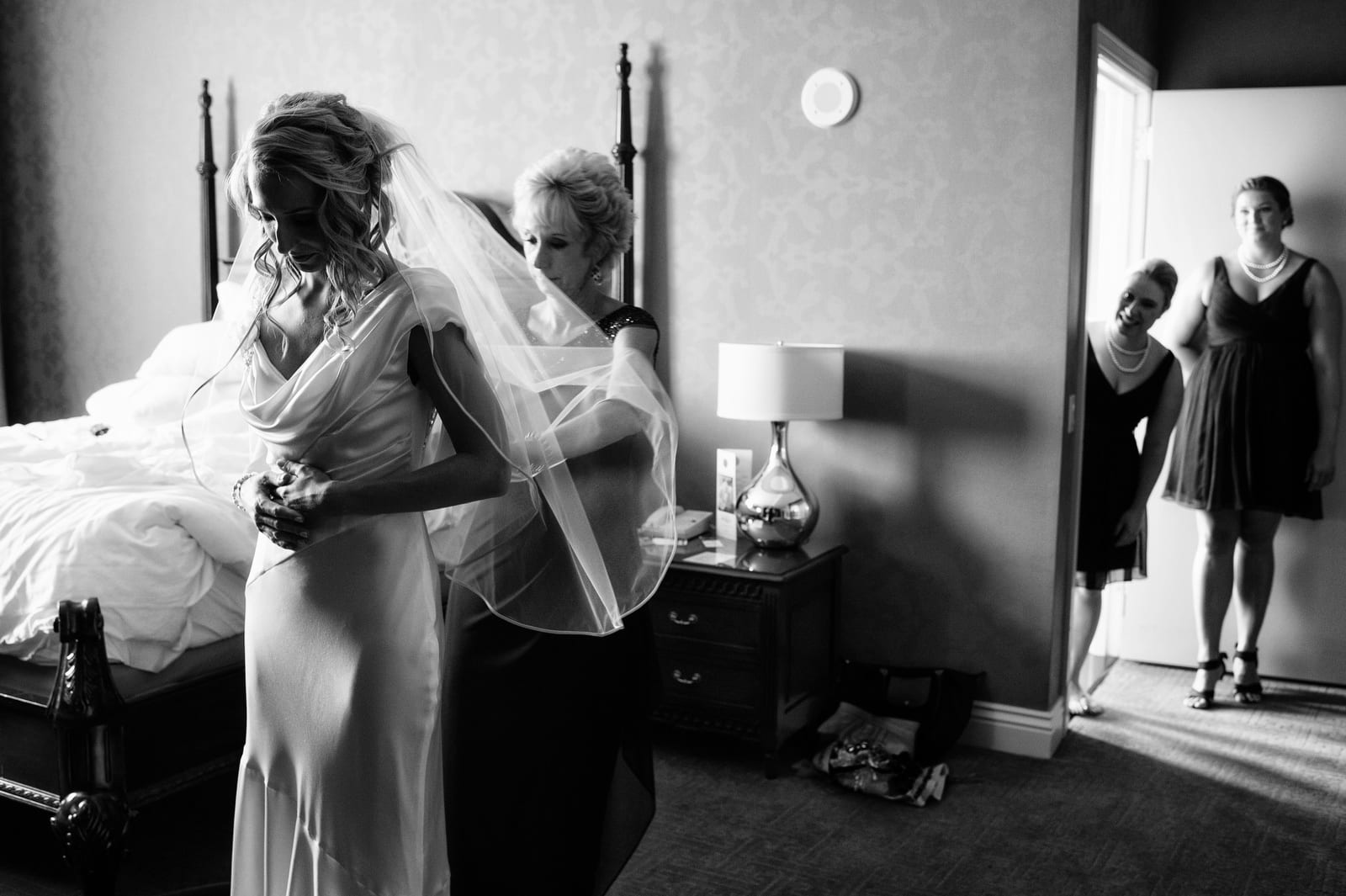 A bride has her dress buttoned up by her mother as bridesmaids peek through the doorway at the Renaissance Hotel Pittsburgh.