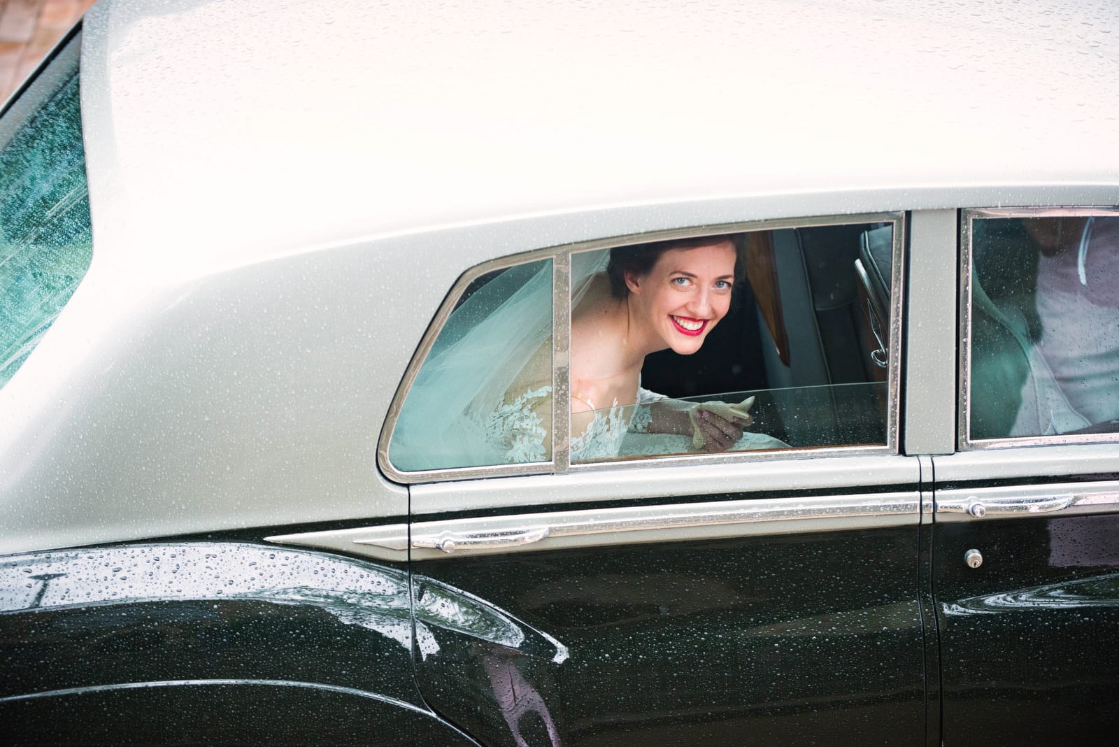 A bride smiles as she looks out of the window of a vintage Rolls Royce limousine before her wedding at the Omni William Penn hotel.