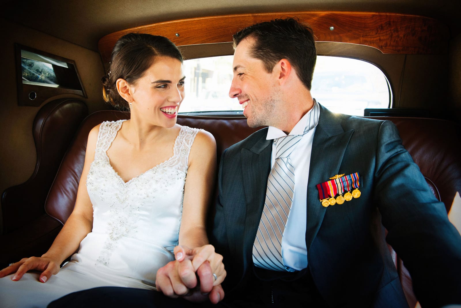 A bride and groom smile and hold hands in the back seat of a vintage Bentley limousine after their wedding at the Cathedral of St. Matthew the Apostle in Washington, DC.