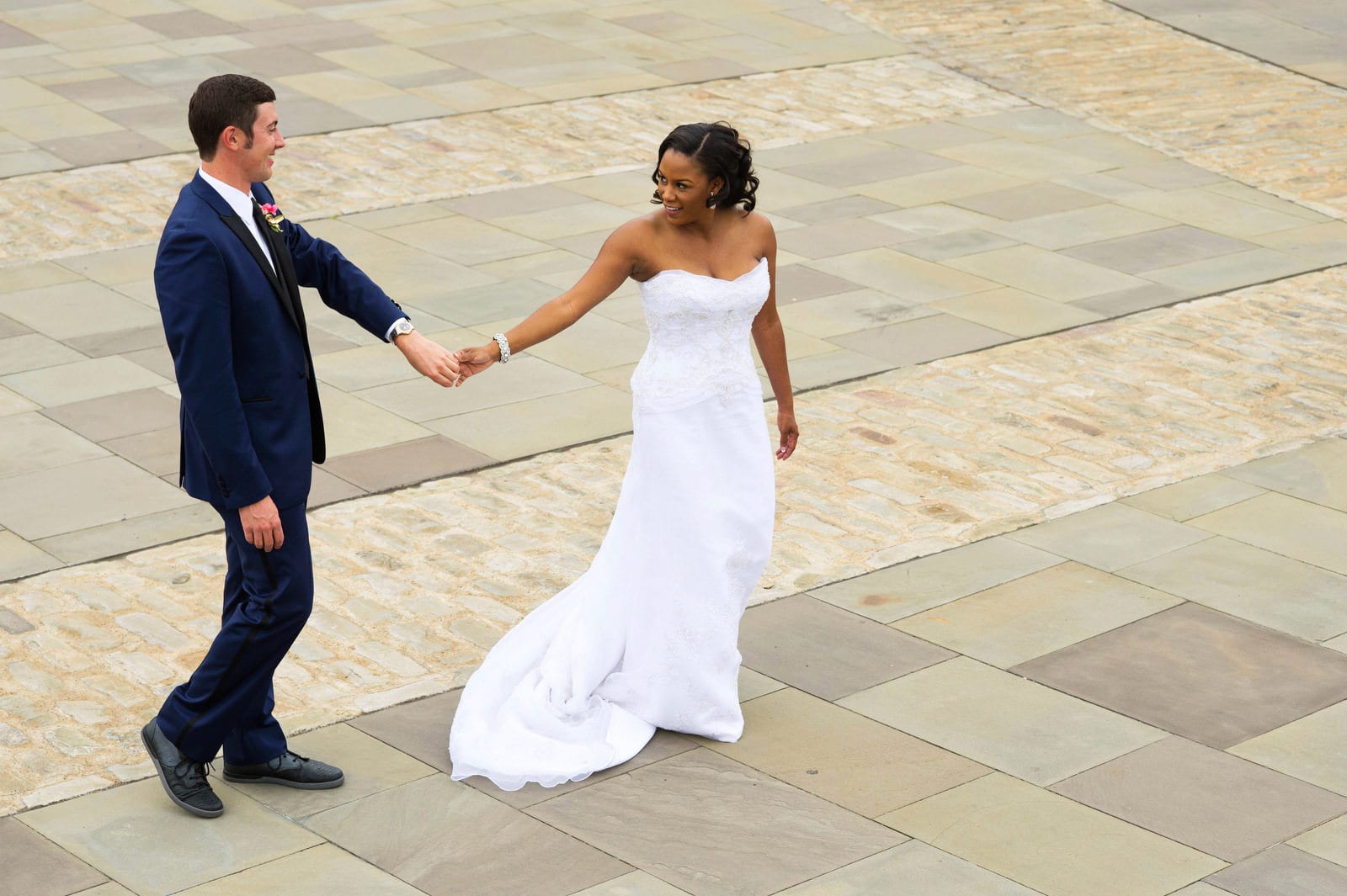 Seen from above, a bride and groom hold hands and walk on the flagstone patio next to the fountain at Point State Park.