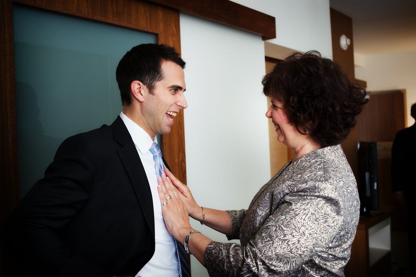 A groom smiles at his mother as she smooths his tie as he gets ready for his Pittsburgh Center for the Arts Wedding.
