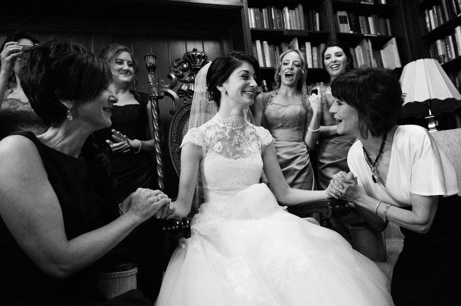 A bride is seated in a chair and is surrounded by her bridesmaids and her mother and mother in law during the bedekken at her Clay Center for the Arts wedding in Charleston West Virginia.
