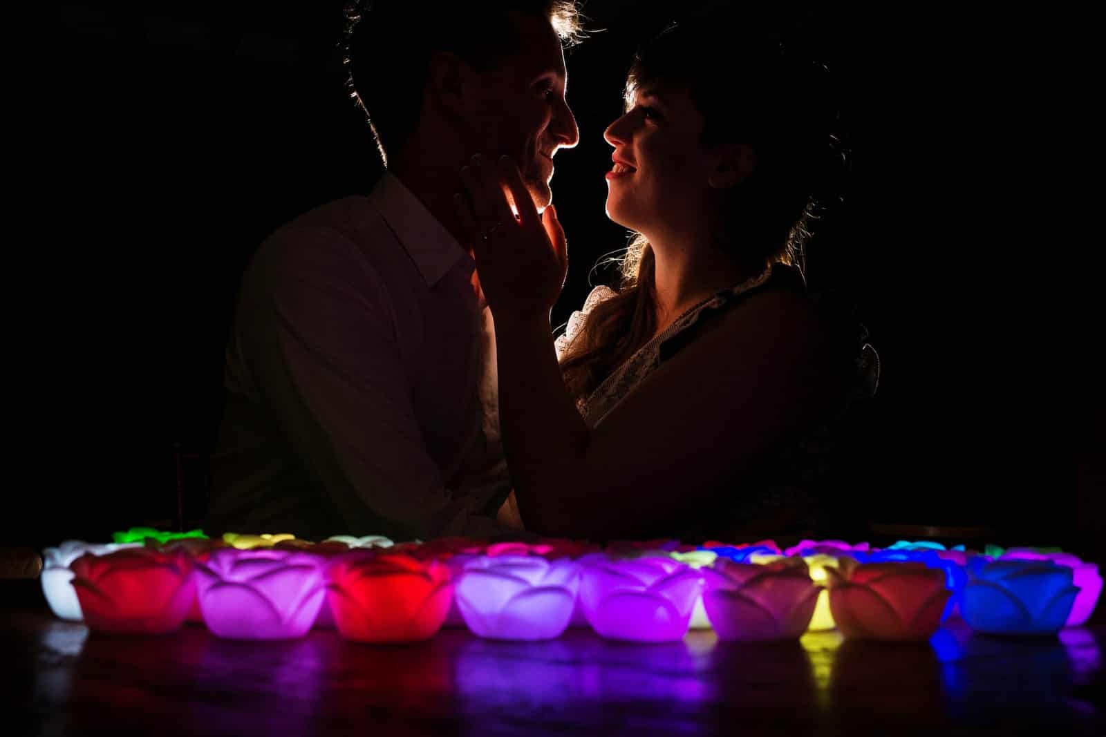 A rim lit couple face each other and smile with a bunch of multi-colored glowing rose lights during their wedding at Lingrow Farm.