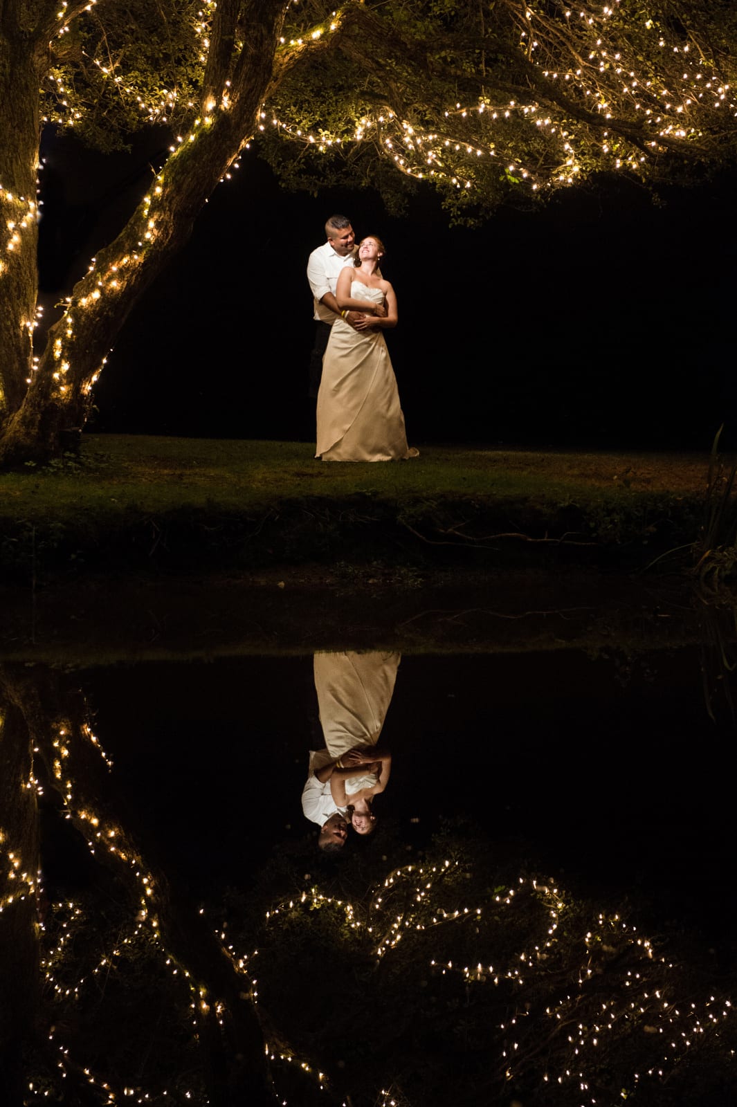 A bride and groom stand beneath a tree with twinkle lights and are reflected in the stream outside of their wedding at Green Gables in Westmoreland County.