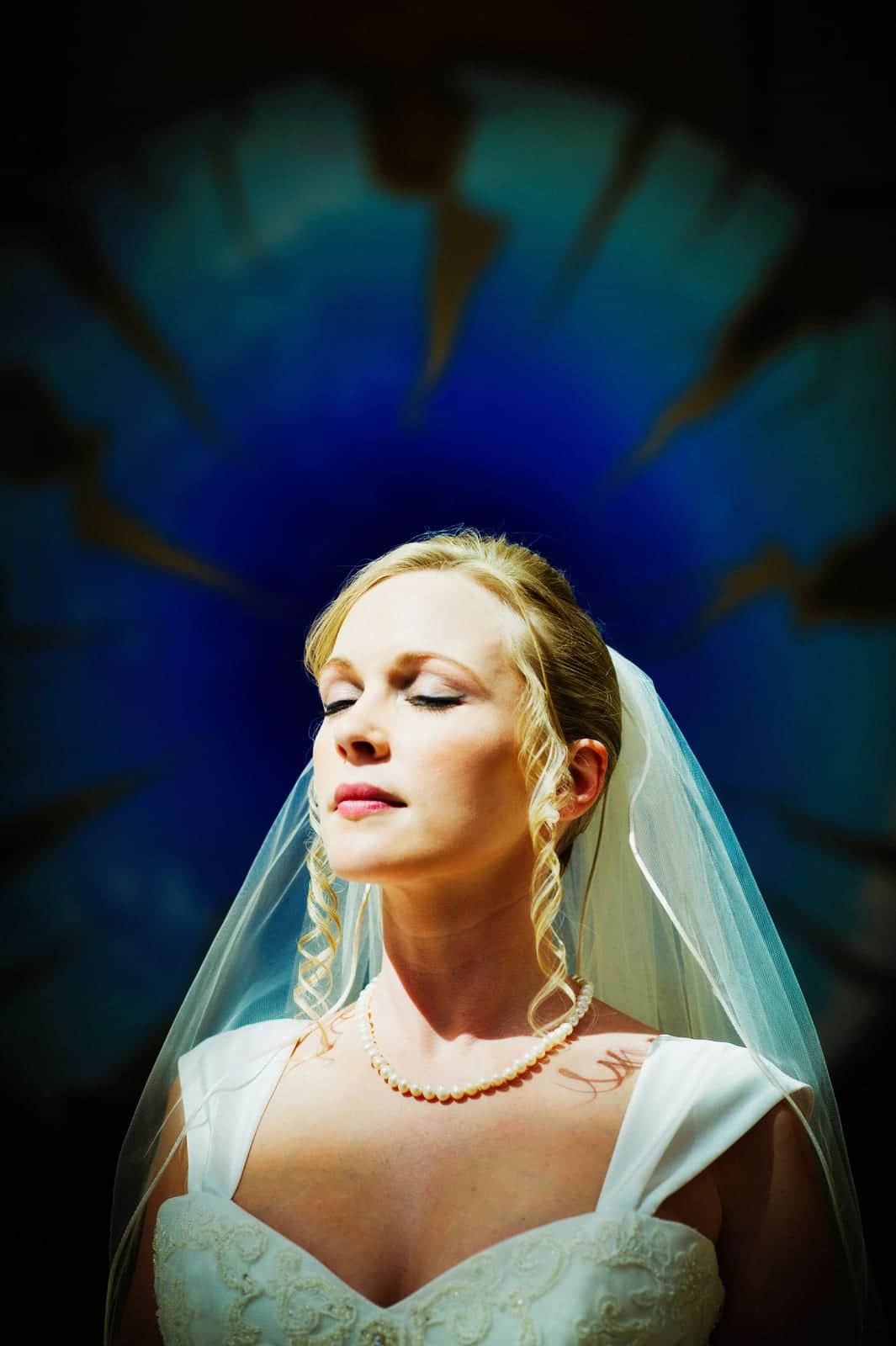 A bride closes her eyes as she faces the sunlight with a blue painting behind her before her Fairmont Hotel Pittsburgh wedding.