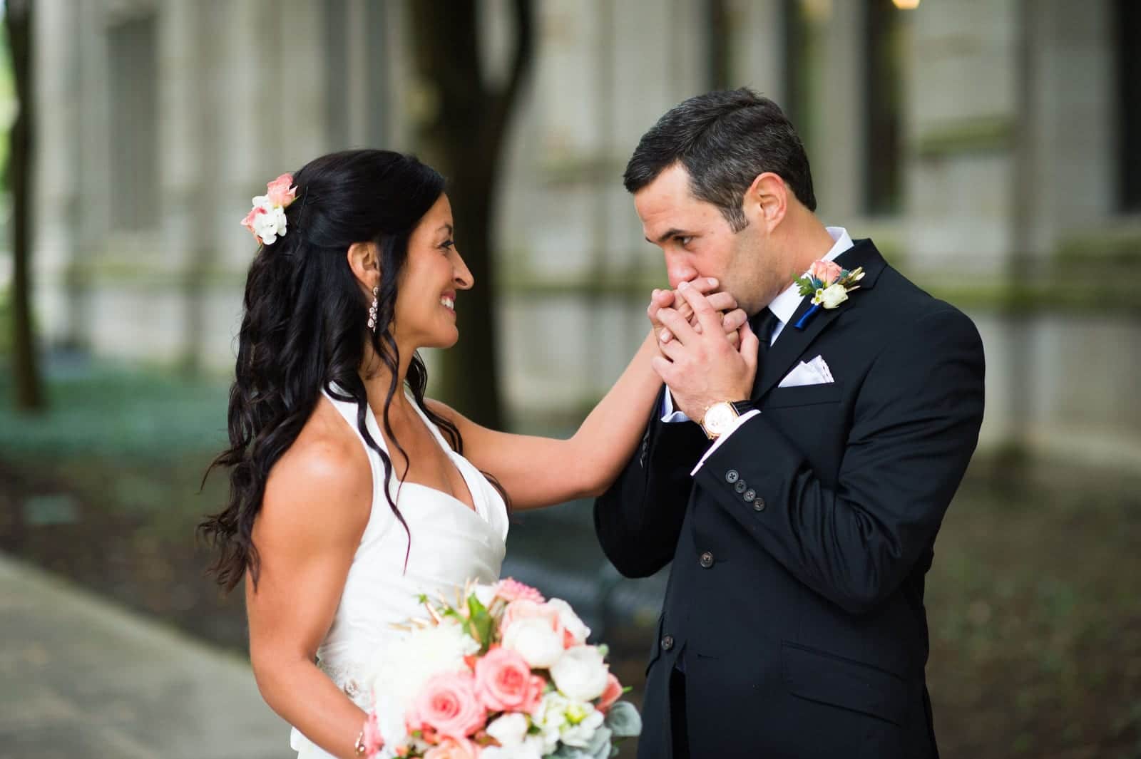 A groom holds his bride's hand to his lips as he kisses it before their Pittsburgh Athletic Association wedding.
