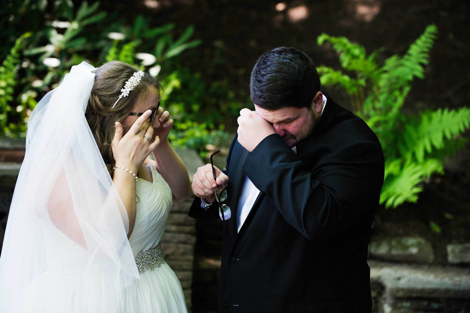 A bride and groom wipe tears from their eyes after having their first look.