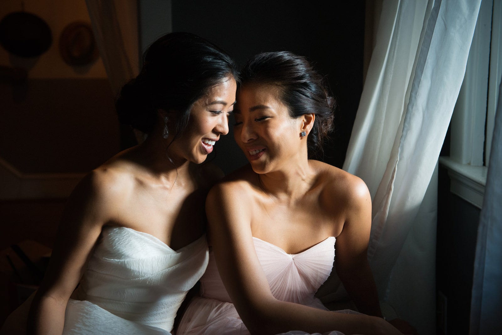 A bride sits forehead-to-forehead with her sister next to a window during a wedding in Washington, DC.